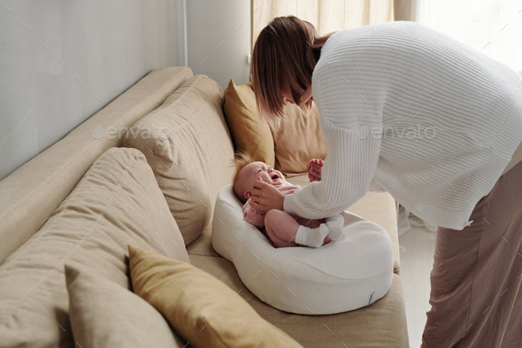 Young woman bending over couch with her cute crying baby daughter
