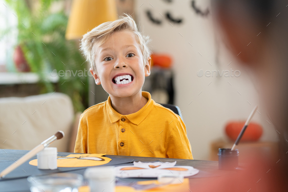Spooky boy with white fangs looking at camera by table