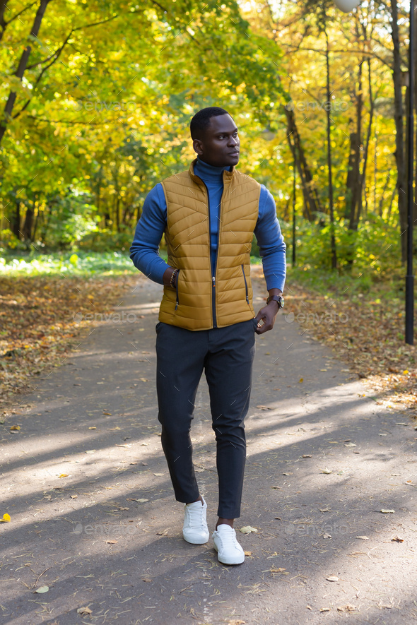 Cheerful african american young man in stylish clothes walks in autumn park on sunny warm autumn day - Stock Photo - Images