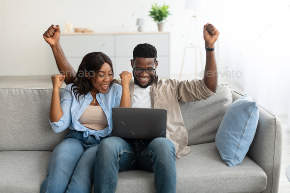 African american couple using laptop, celebrating win