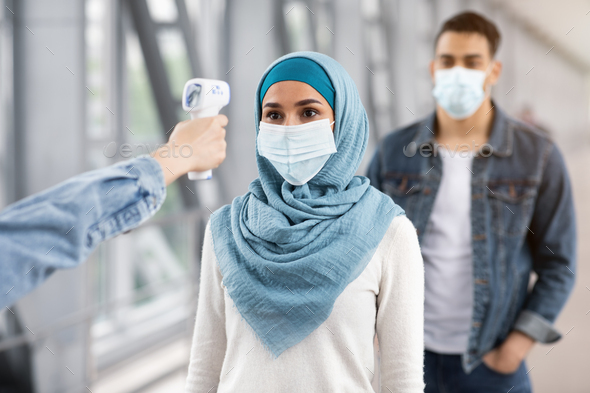 Flying During Coronavirus. Airport Staff Checking Muslim Female Passenger Temperature At Terminal