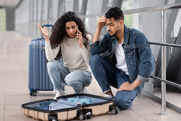 Wrong Suitcase. Shocked middle eastern couple sitting with opened luggage in airport terminal