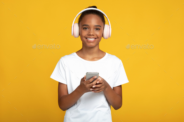 Glad teen black girl pupil in white t-shirt and wireless headphones listen lesson, learn language