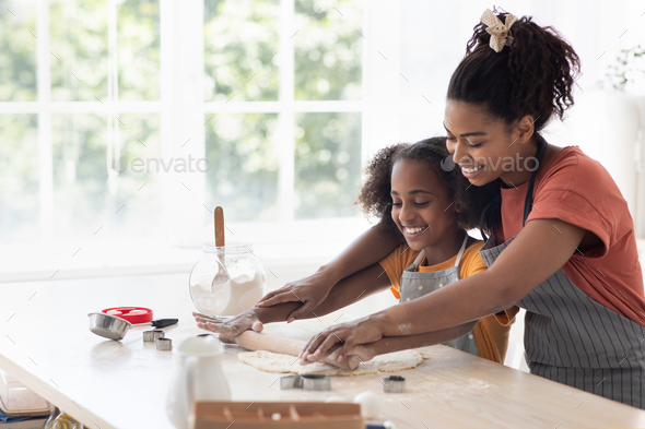 Cheerful black mother helping daughter rolling pasrty dough - Stock Photo - Images