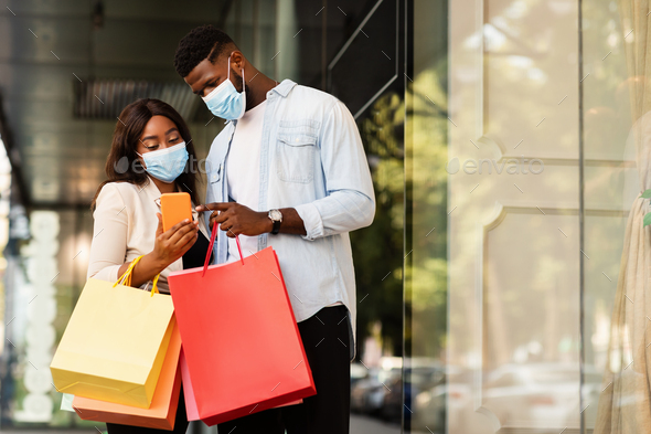 Portrait of black couple using cellphone wearing masks near mall - Stock Photo - Images