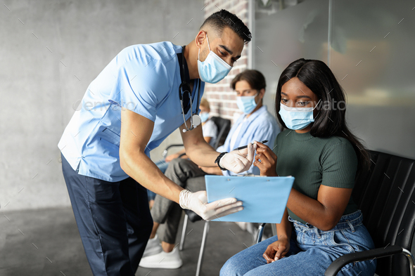 Black lady in face mask signing medical file before vaccination - Stock Photo - Images