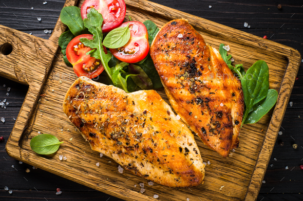 Grilled chicken fillet at wooden cutting board with vegetables Stock Photo  by Nadianb