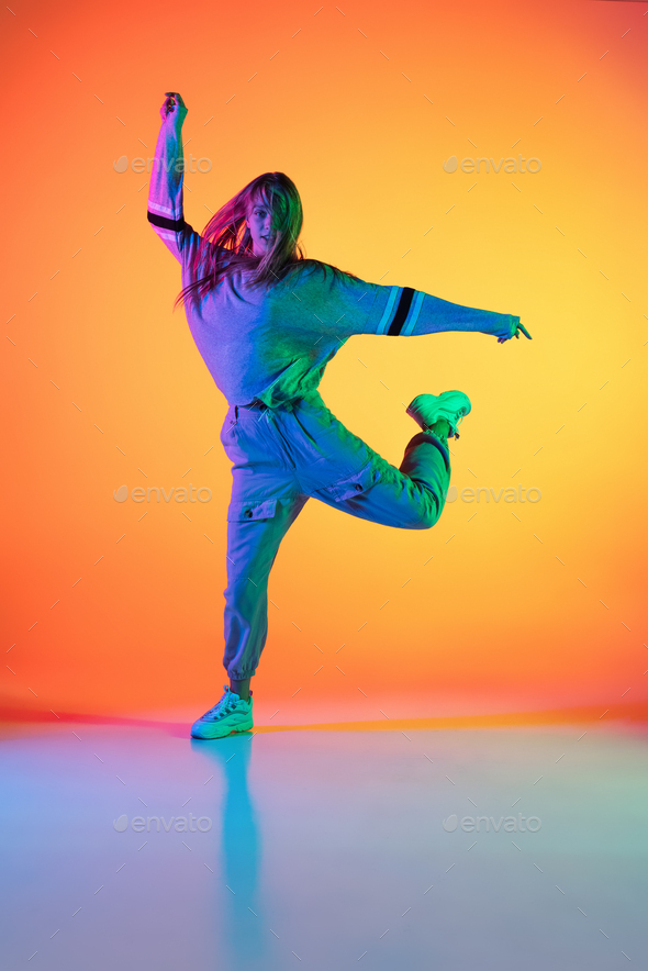 Portrait of young sportive girl dancing hip-hop in stylish clothes on colorful background at dance