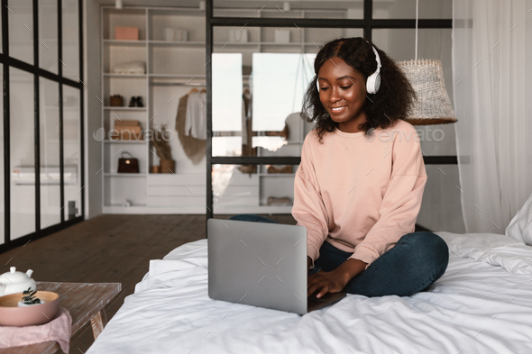 African Female Using Laptop Wearing Headphones Working Online At Home - Stock Photo - Images