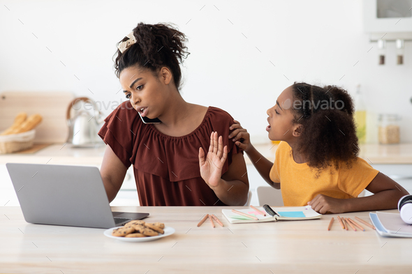 Angry teen girl sitting by working mom, kitchen interior - Stock Photo - Images