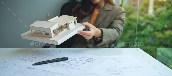 An architect holding and working on an architecture house model with shop drawing paper