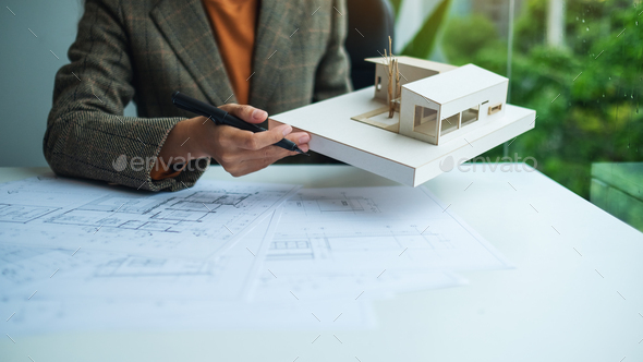 A female architect holding and working on an architecture house model with shop drawing paper