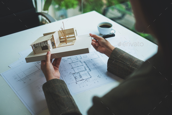 An architect holding and working on an architecture house model with shop drawing paper