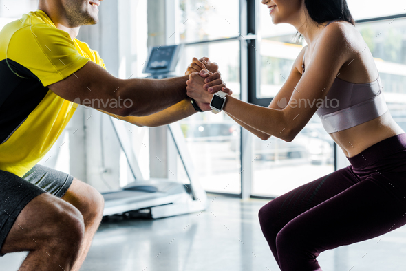 cropped view of sportsman and sportswoman doing squat together in sports center