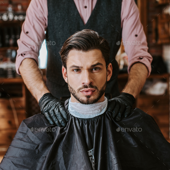 barber in black latex gloves putting hands on shoulders of man in