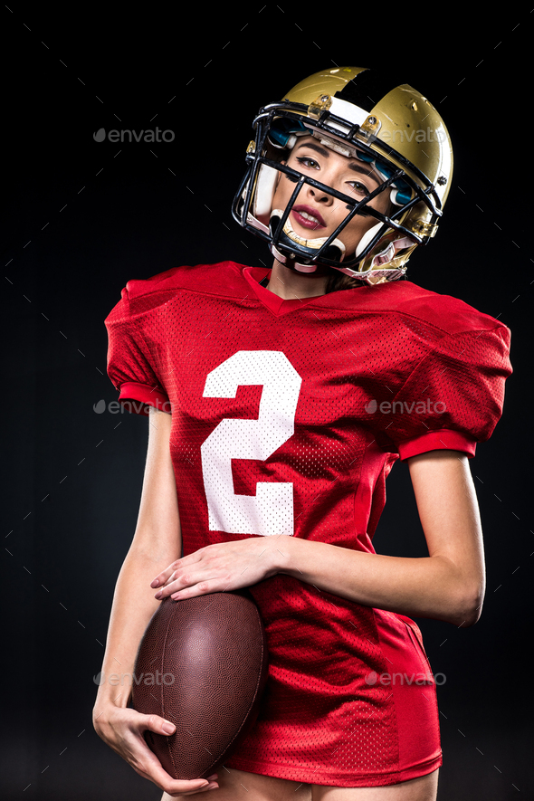 Beautiful woman in uniform playing american football with ball on