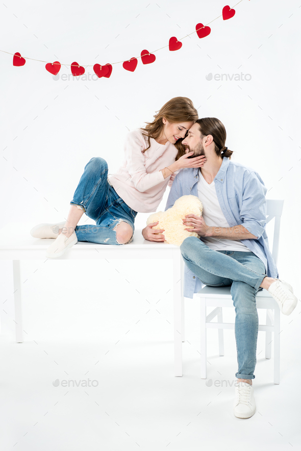Beautiful young couple in love sitting on white furniture with heart