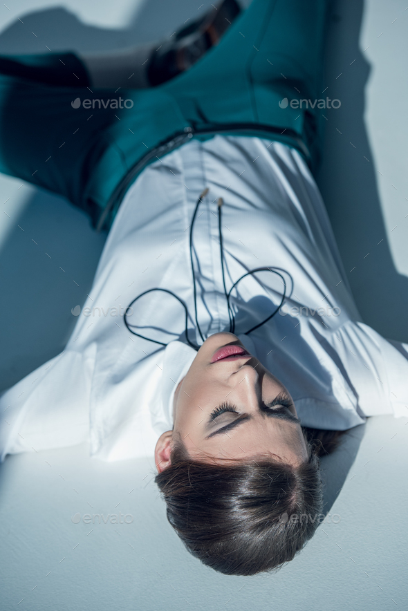 young stylish hipster woman in white shirt and green trousers lying on floor with closed eyes
