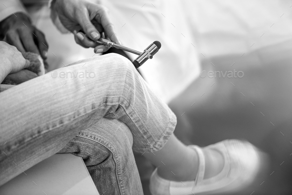 partial view of doctor examining girl patient with reflex hammer, black and white photo
