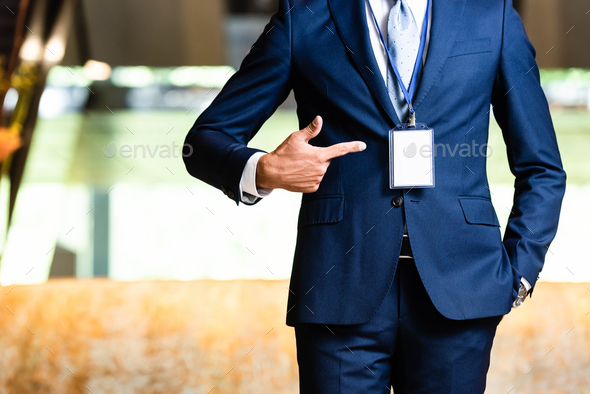 cropped view of man in suit pointing with finger at badge