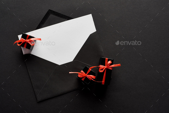 top view of black envelope with blank card near decorative gift boxes on black background