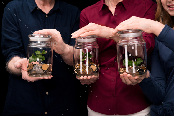 grandchild, grandfather and grandmother holding jars with money and plants isolated on black in