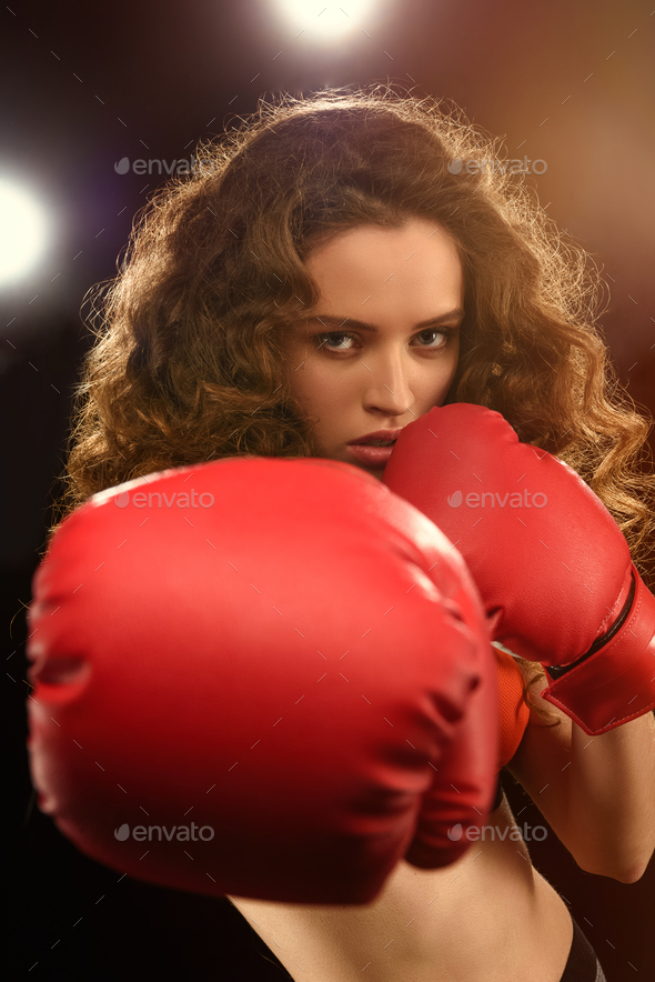 Beautiful young sportswoman in boxing gloves punching at camera
