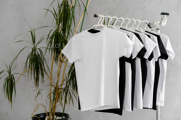 Row of white t-shirts on hangers on rack Stock Photo by FabrikaPhoto