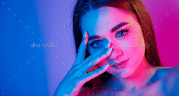 Neutral facial expression. Fashionable young woman standing in the studio with neon light