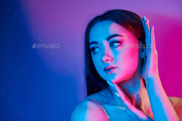 Neutral facial expression. Fashionable young woman standing in the studio with neon light