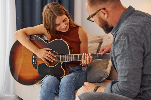Private lesson. Guitar teacher showing how to play the instrument to young woman