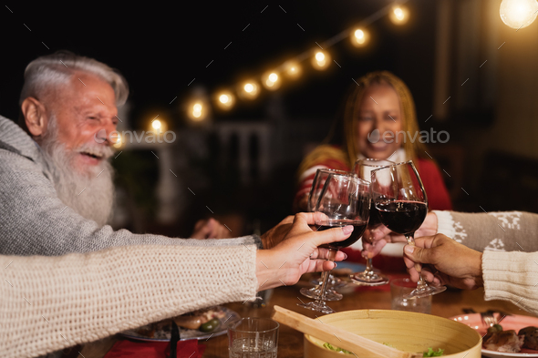 Happy multiracial seniors toasting with red wine glasses and celebrating holidays on house patio - Stock Photo - Images