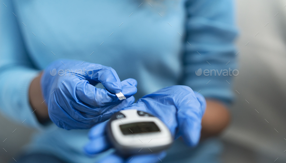 Young nurse checking glycemia test for diabetes while wearing surgical gloves - Stock Photo - Images
