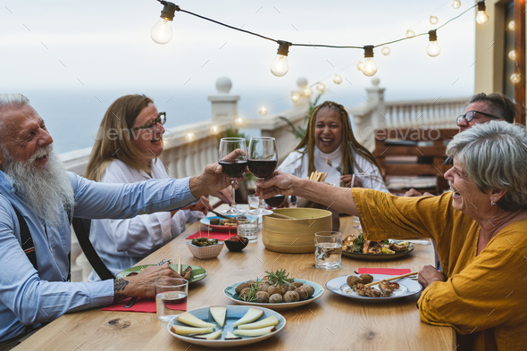 Multiracial senior friends having fun dining together and toasting with red wine on house patio - Stock Photo - Images