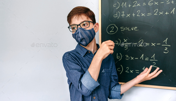 Boy with mask solving math exercises on blackboard