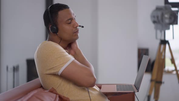 Side View of Young Man Stretching Neck Spasm Typing on Laptop Keyboard in Home Office alt