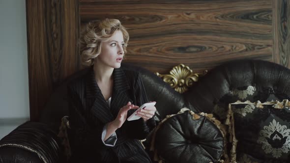 Lady Sitting on Luxury Sofa Typing on Smartphone and Looking Aside in Room alt
