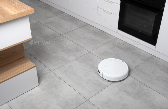 Washing White robot vacuum cleaner on a concrete tile floor cleaning dust. Smart Electronic