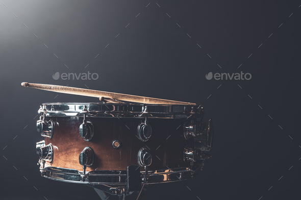 Close-up snare drum and drum sticks on a dark background.