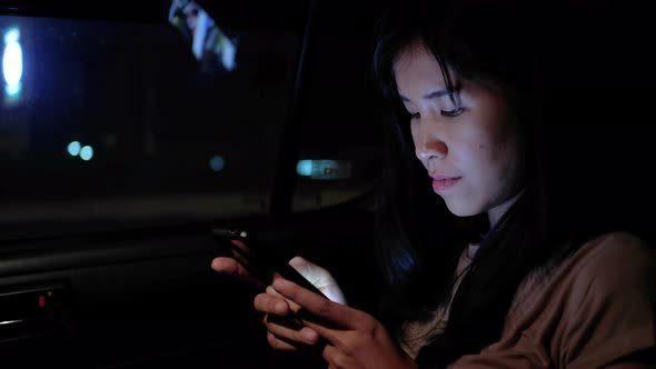 Asian young woman using smartphone in a car, checking mails, chats or the news online. alt