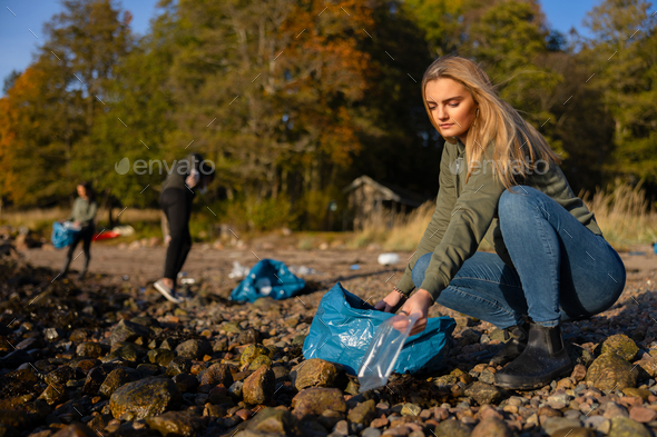 Serious young woman in environment conservation team picking up plastic at beach - Stock Photo - Images
