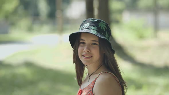 A Teenage Girl in a Panama Hat is Walking Through the Park in the Summer alt