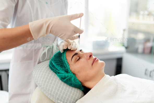 Beautician injects rejuvenation cosmetic preparations into the woman's forehead.