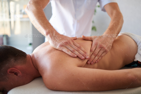 Closeup of man massaging his client's back with his hands in massage cabinet - Stock Photo - Images