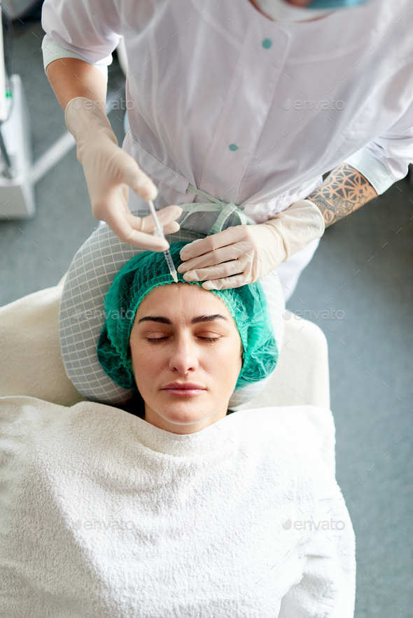 A cosmetologist injects rejuvenation cosmetic preparation into a woman's face.