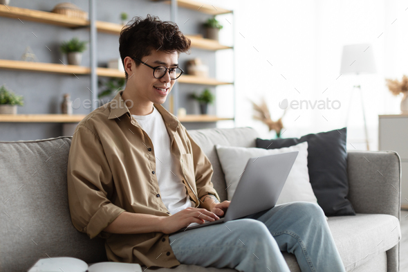 Smiling asian man working on laptop at home - Stock Photo - Images