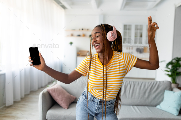 Joyful afro american long-haired woman singing and dancing, using smartphone - Stock Photo - Images