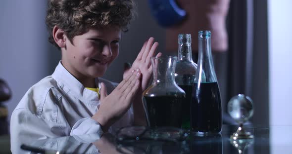 Close-up Side View of Strange Caucasian Boy Rubbing Hands and Looking at Flasks with Liquids. Young alt