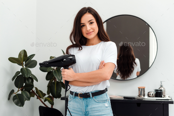 A professional hairdresser stands in a beauty salon with a hairdryer in hand