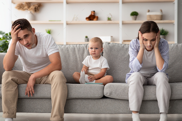 Family Conflicts. Cute infant baby sitting between offended parents after quarrel - Stock Photo - Images